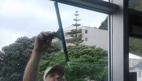 Window Cleaner using a squeegee reaching up with one hand