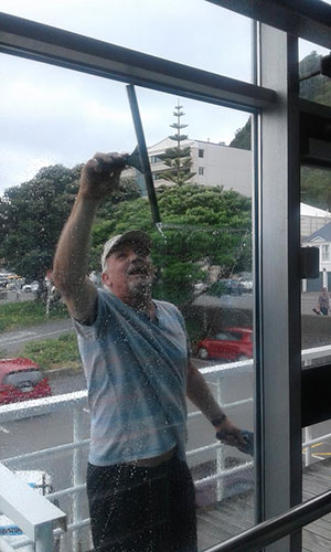 Window Cleaner using a squeegee reaching up with one hand