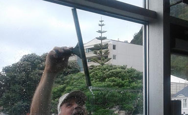 Window Cleaner using a squeegee reaching up with one hand