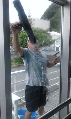 Window Cleaner using a t-bar washer reaching up with one hand